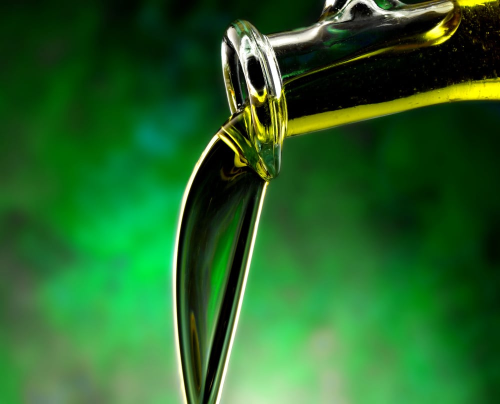 olio di sansa di oliva che cade da una bottiglia con sfondo verde